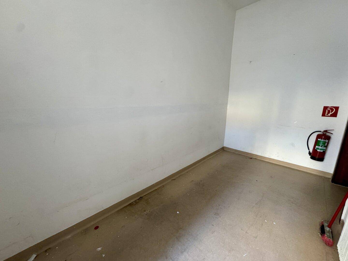 Leere Raumecke mit einfachem Boden und einem Feuerlöscher an der Wand, bereit zur Nutzung.