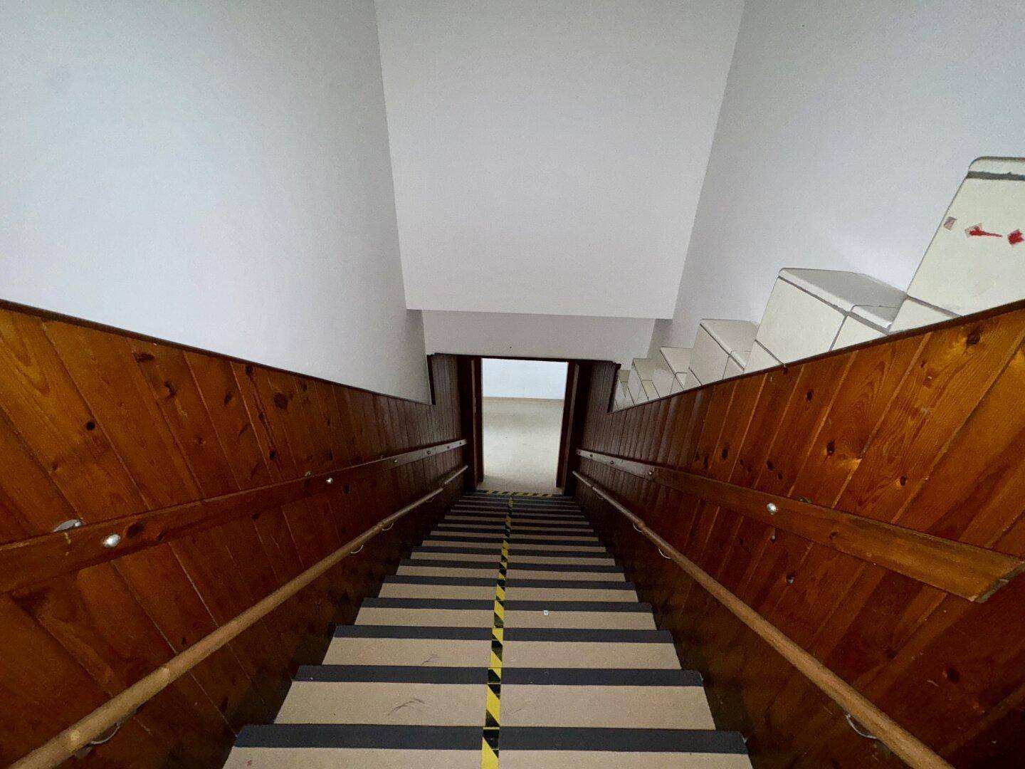Treppenhaus mit Holzvertäfelung und Handläufen, die Stufen sind mit Sicherheitsmarkierungen versehen.