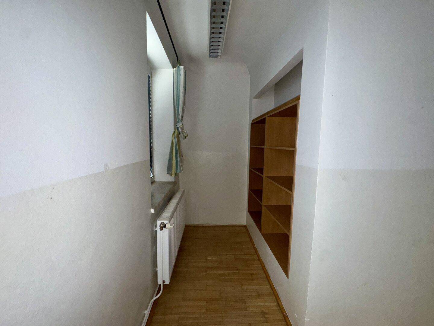 Schmaler Flur mit Fenster, Heizkörper und praktischen eingebauten Holzregalen für Stauraum.
