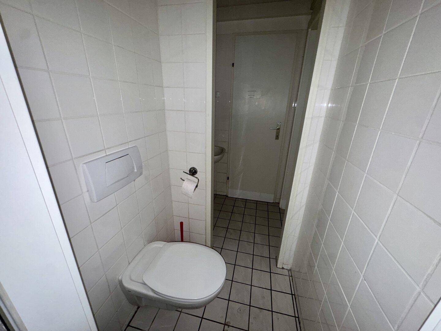 Kleiner Toilettenraum mit weißen Fliesen, wandhängendem WC und dunklem Fliesenboden.