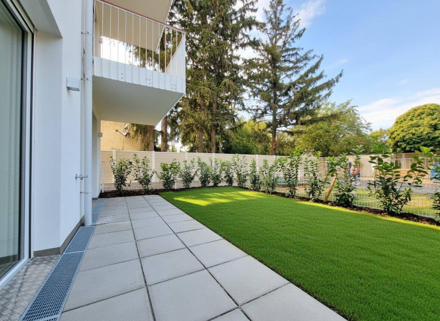 Helle Terrasse mit Steinplatten und angrenzendem Rasen, ideal für entspannte Stunden im Freien.
