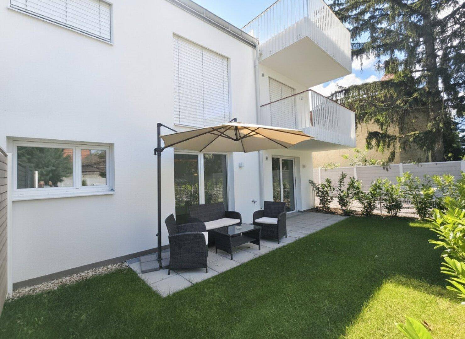 Gemütliche Terrasse mit Gartenmöbeln und Sonnenschirm, direkt am gepflegten Rasen gelegen.