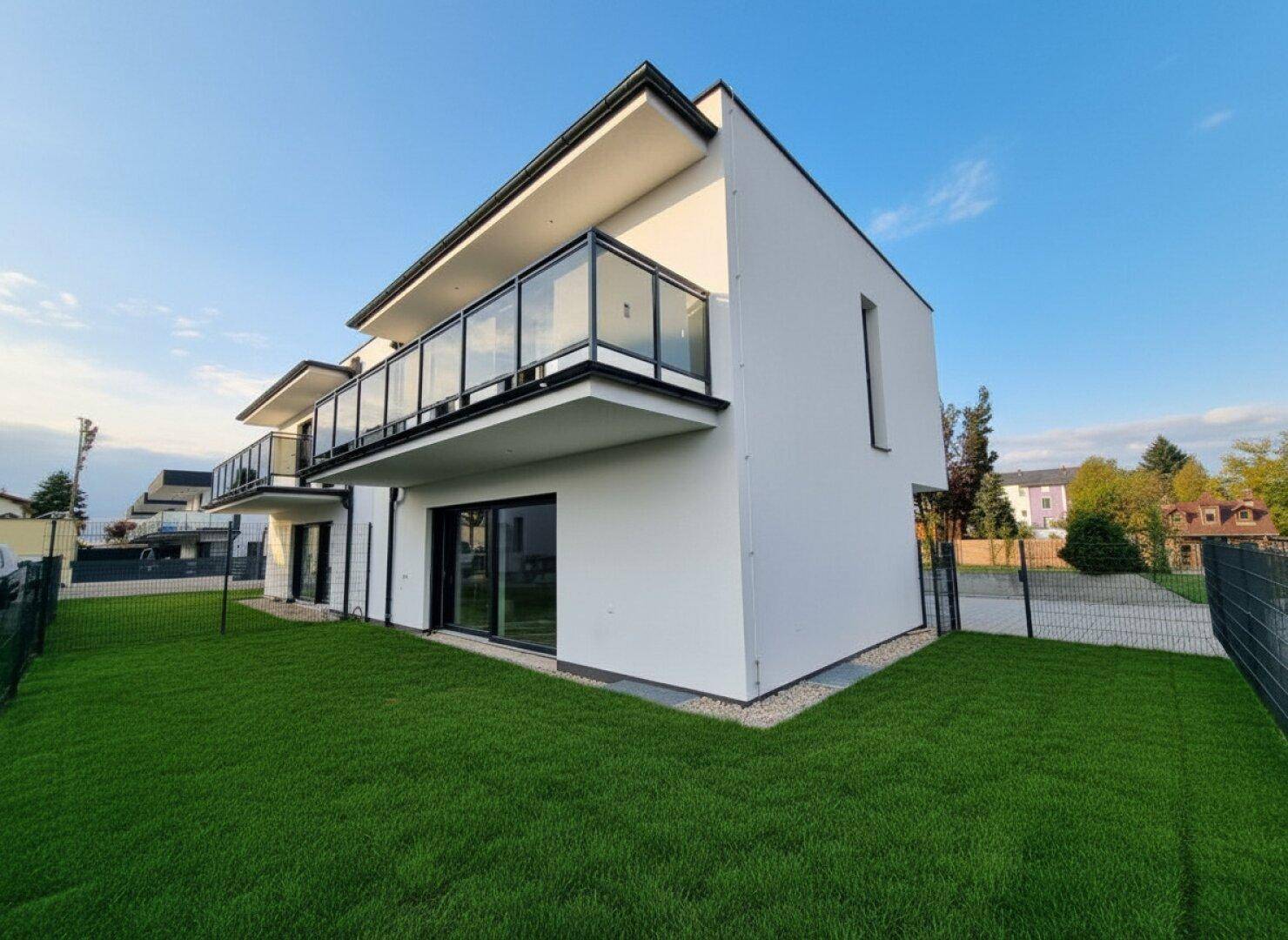 Moderne Architektur eines Neubaus mit Balkonen, großen Fenstern und gepflegtem Rasen.
