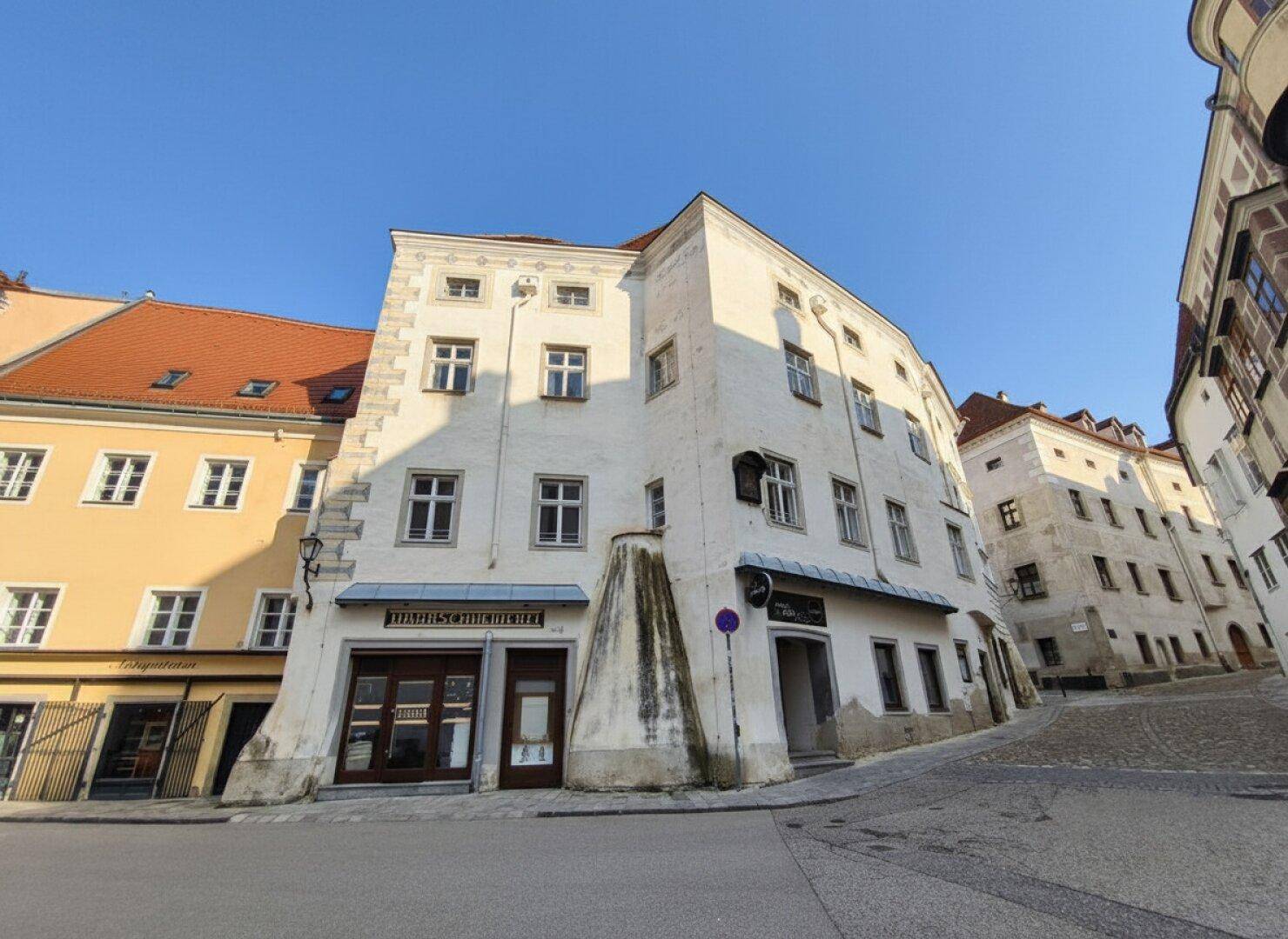 Historisches Gebäude mit weißer Fassade und markanter Architektur an einer gepflasterten Straße.