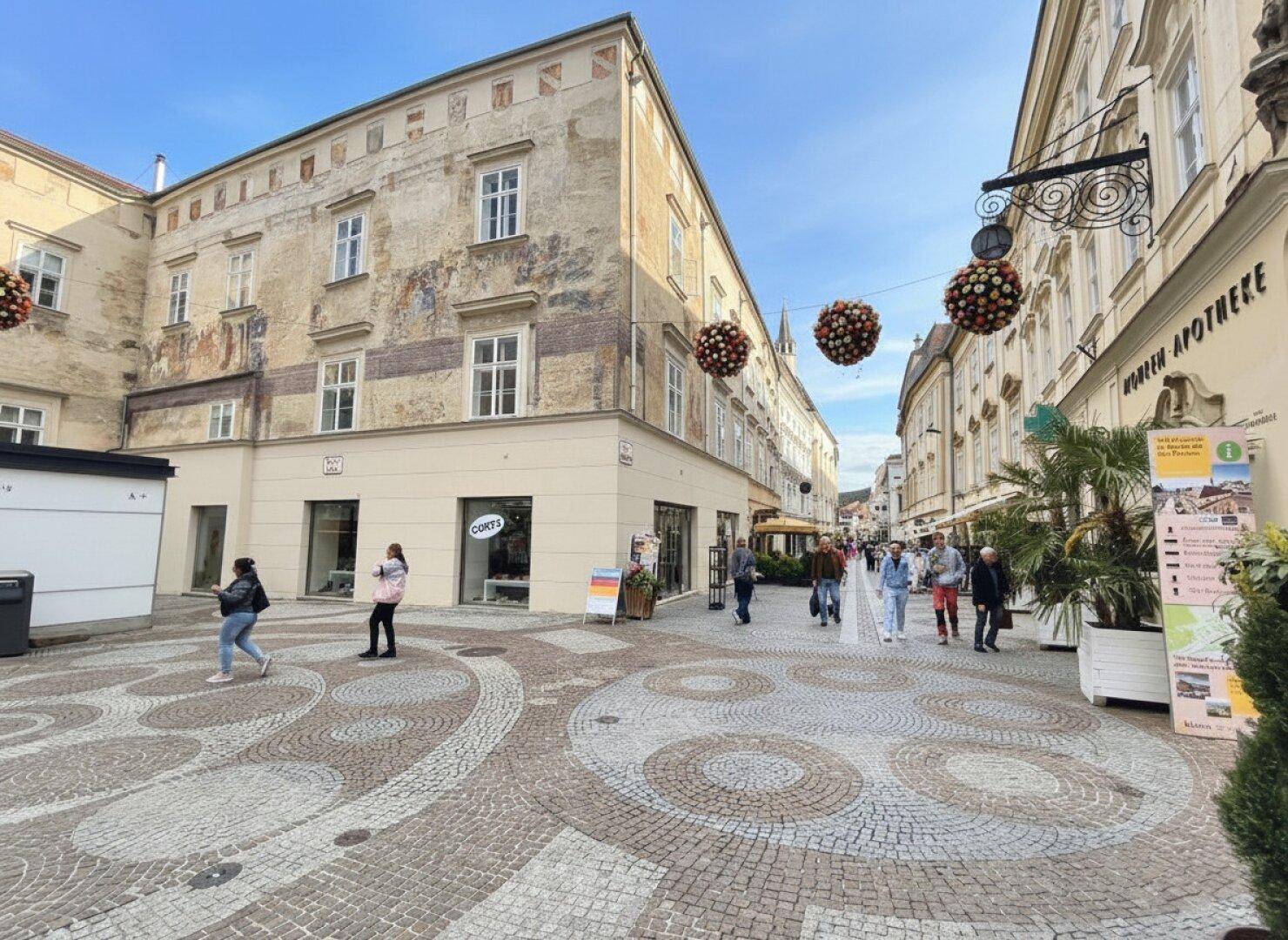 Historische Gebäude entlang einer belebten Straße mit Fußgängern und dekorativen Elementen.