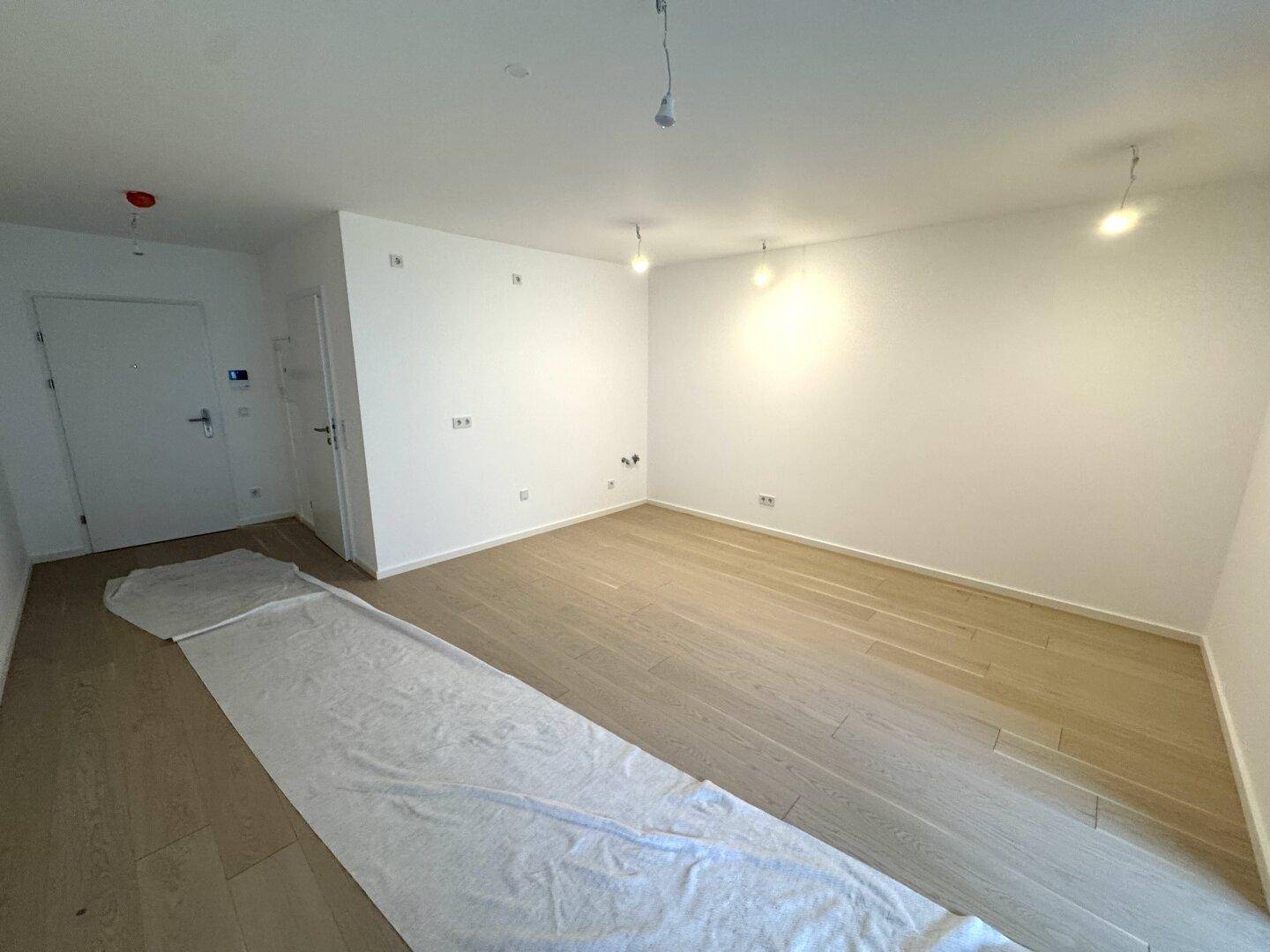 Geräumiger, heller Raum mit Holzboden und weiß gestrichenen Wänden, bereit zum Einzug.