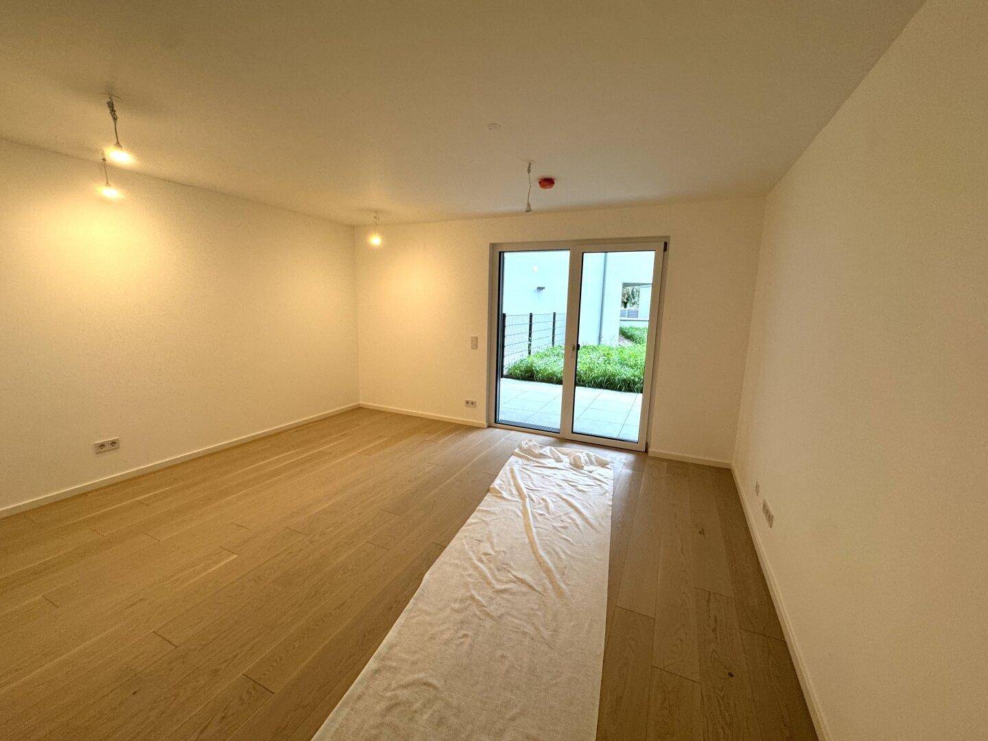 Heller, leerer Raum mit Holzboden und Zugang zu einer Terrasse oder einem Gartenbereich.