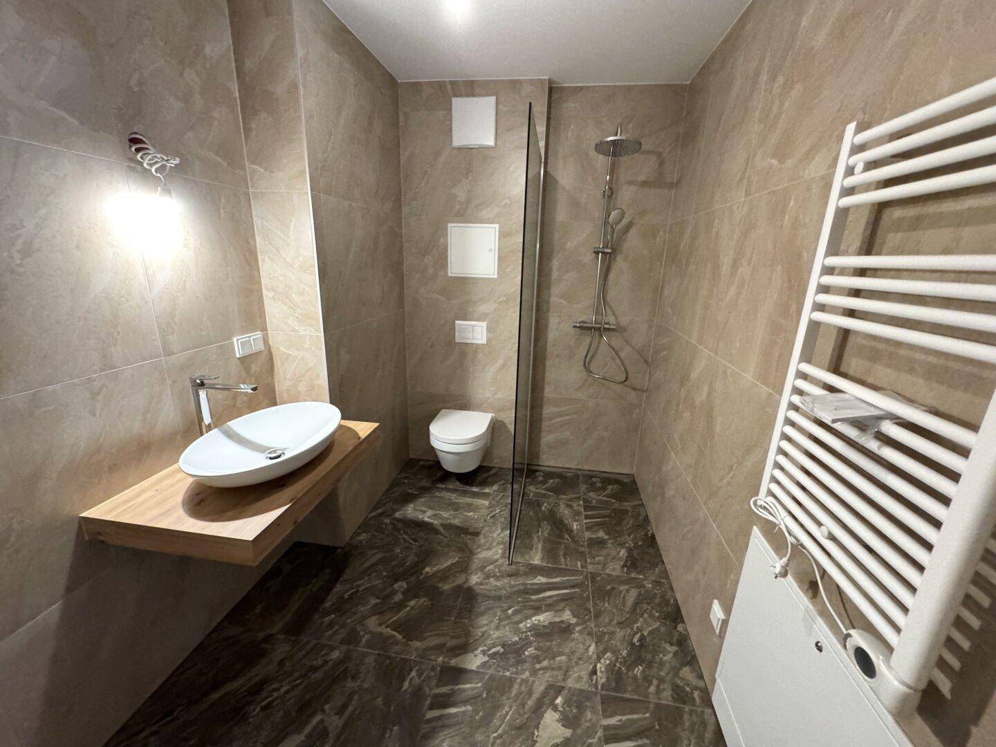 Modernes Badezimmer mit begehbarer Dusche, stilvollem Waschbecken und beheiztem Handtuchhalter.