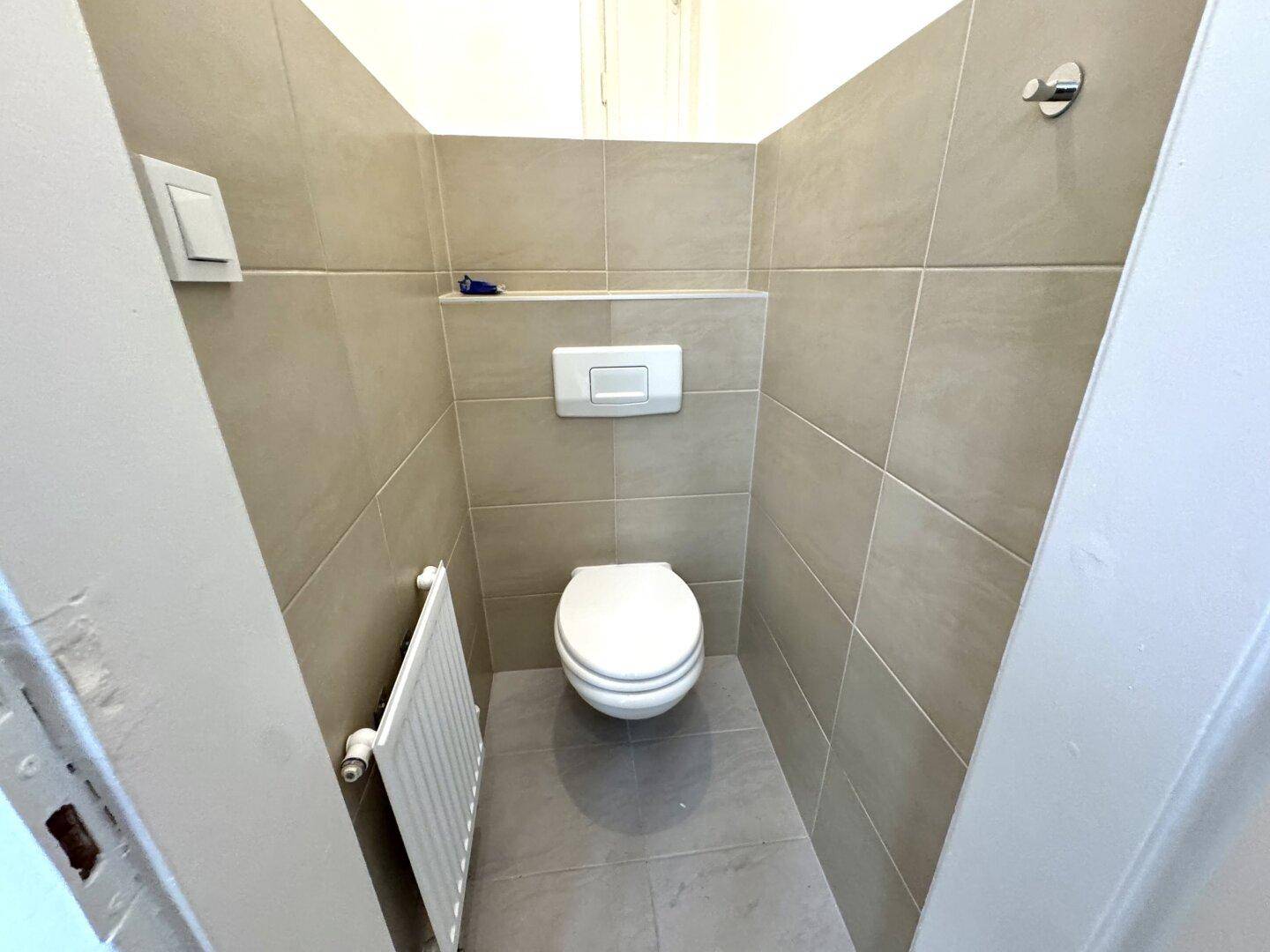 Modern gefliestes Gäste-WC mit wandhängender Toilette und Heizkörper.