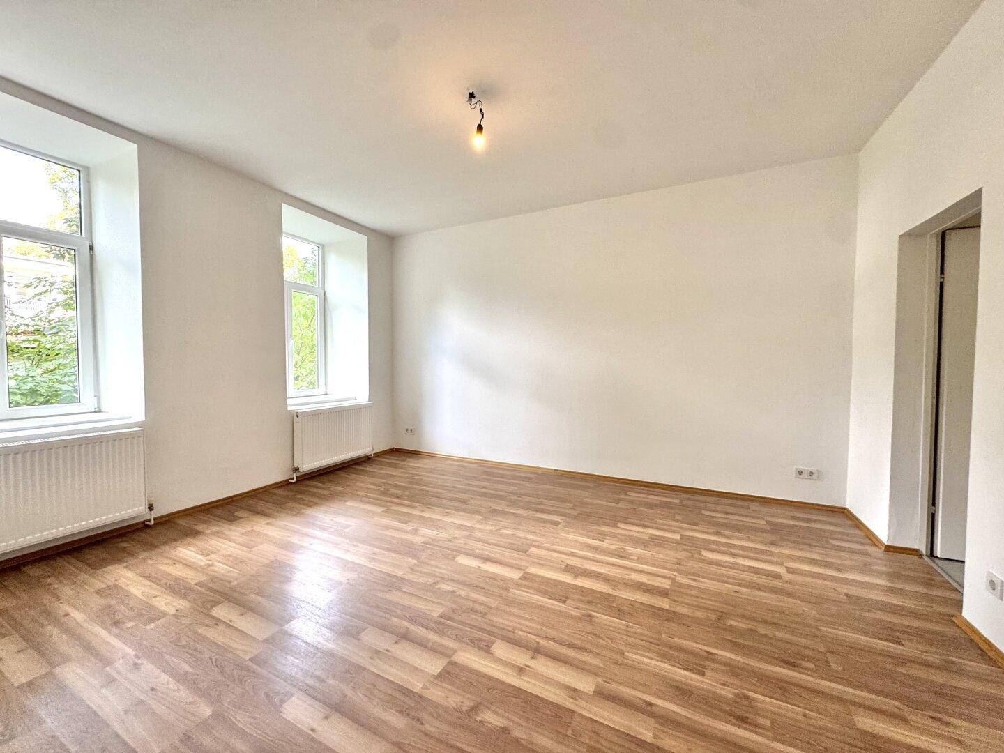 Geräumiges, helles Zimmer mit Holzboden und zwei großen Fenstern.
