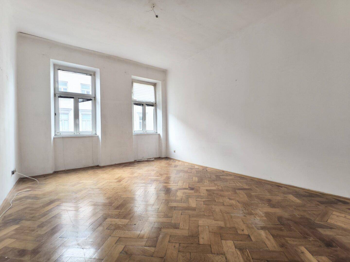 Leerer Raum mit Fischgrätparkett und zwei Fenstern, bereit für die individuelle Gestaltung.