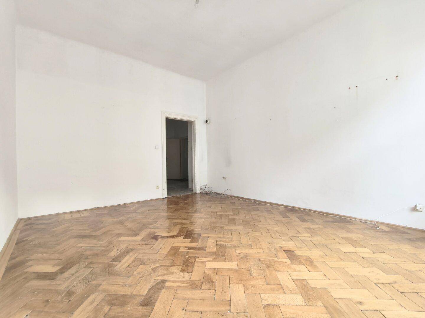 Leerer Raum mit Fischgrätparkett und Türöffnung zu einem weiteren Zimmer.