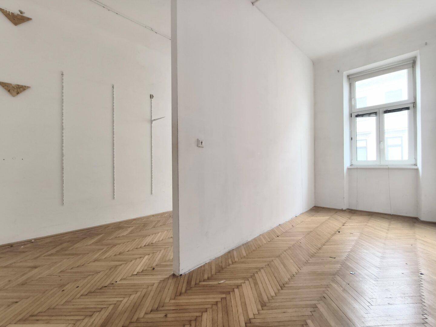 Geräumiger leerer Raum mit Fischgrätparkett und einer Trennwand, die den Bereich gliedert.