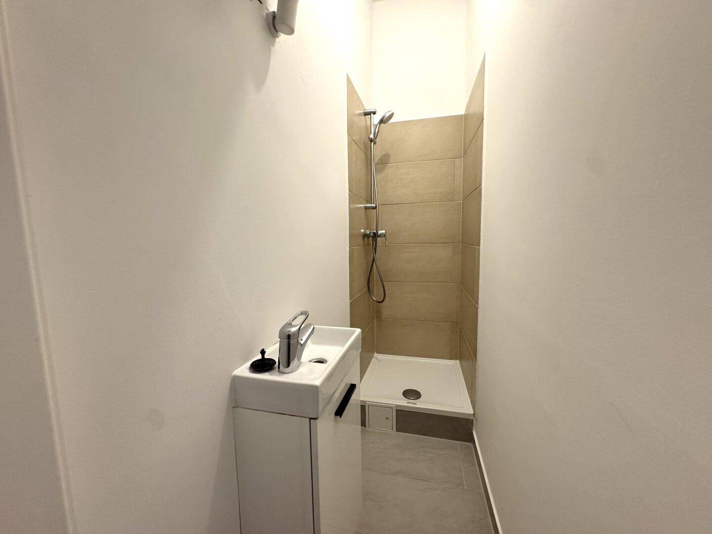 Kleines Badezimmer mit Dusche und modernem Waschbecken, funktional und hell gestaltet.