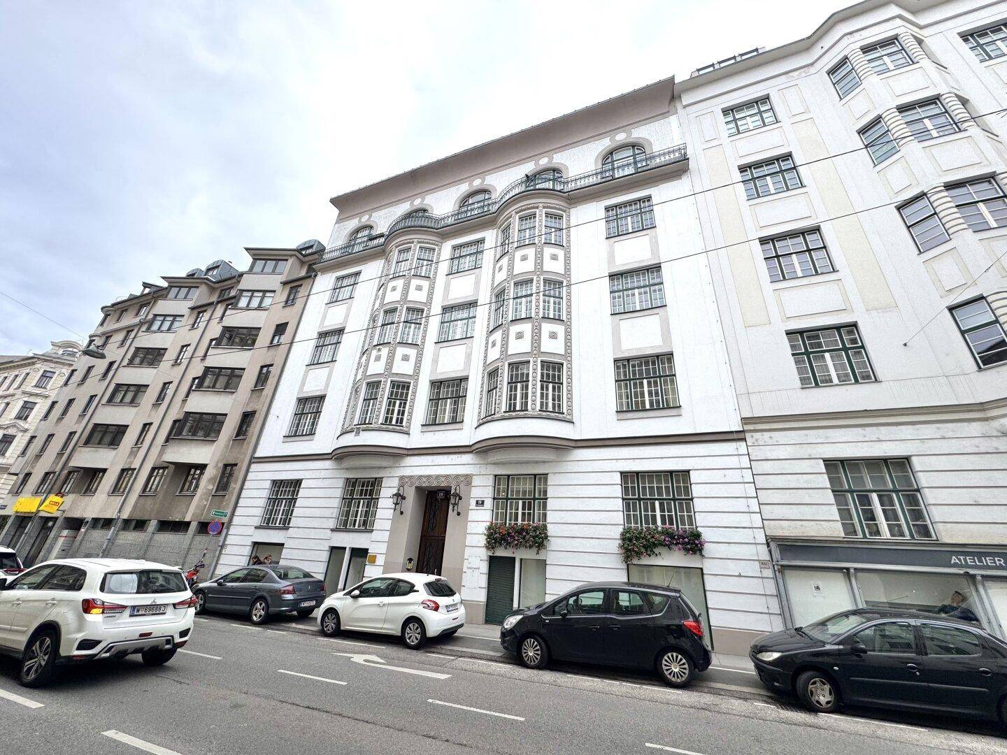 Historische Fassade eines Altbaus mit vielen Fenstern und geparkten Autos auf der Straße.
