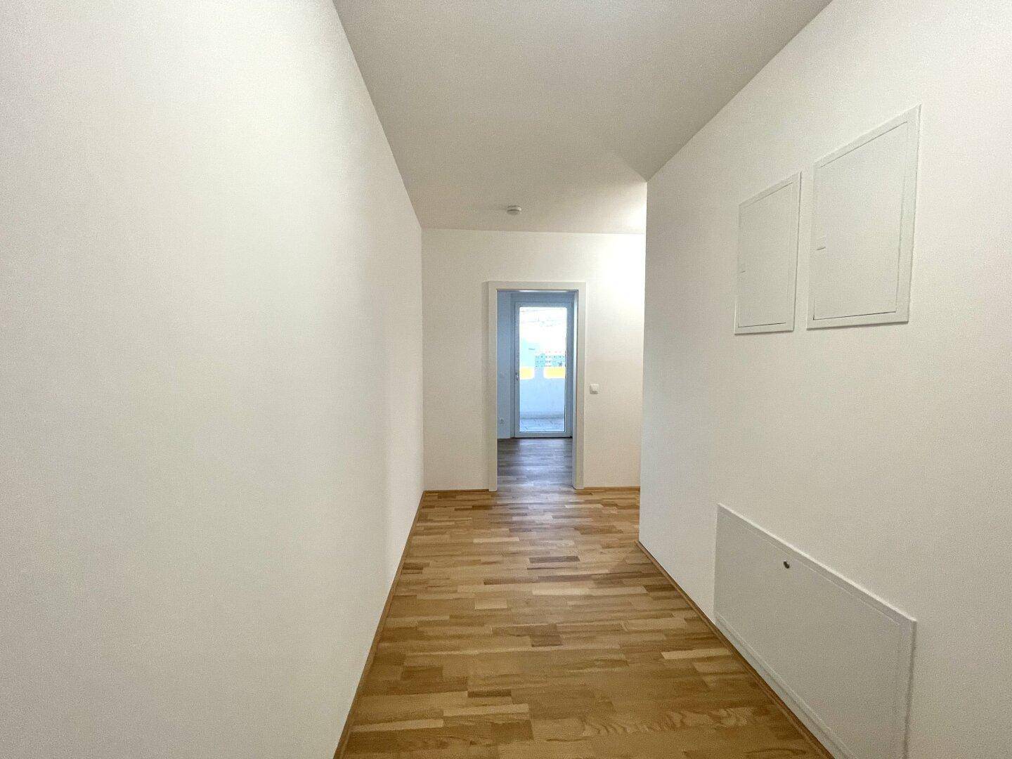 Heller Flur mit Parkettboden und weißen Wänden, der zu weiteren Räumen führt.