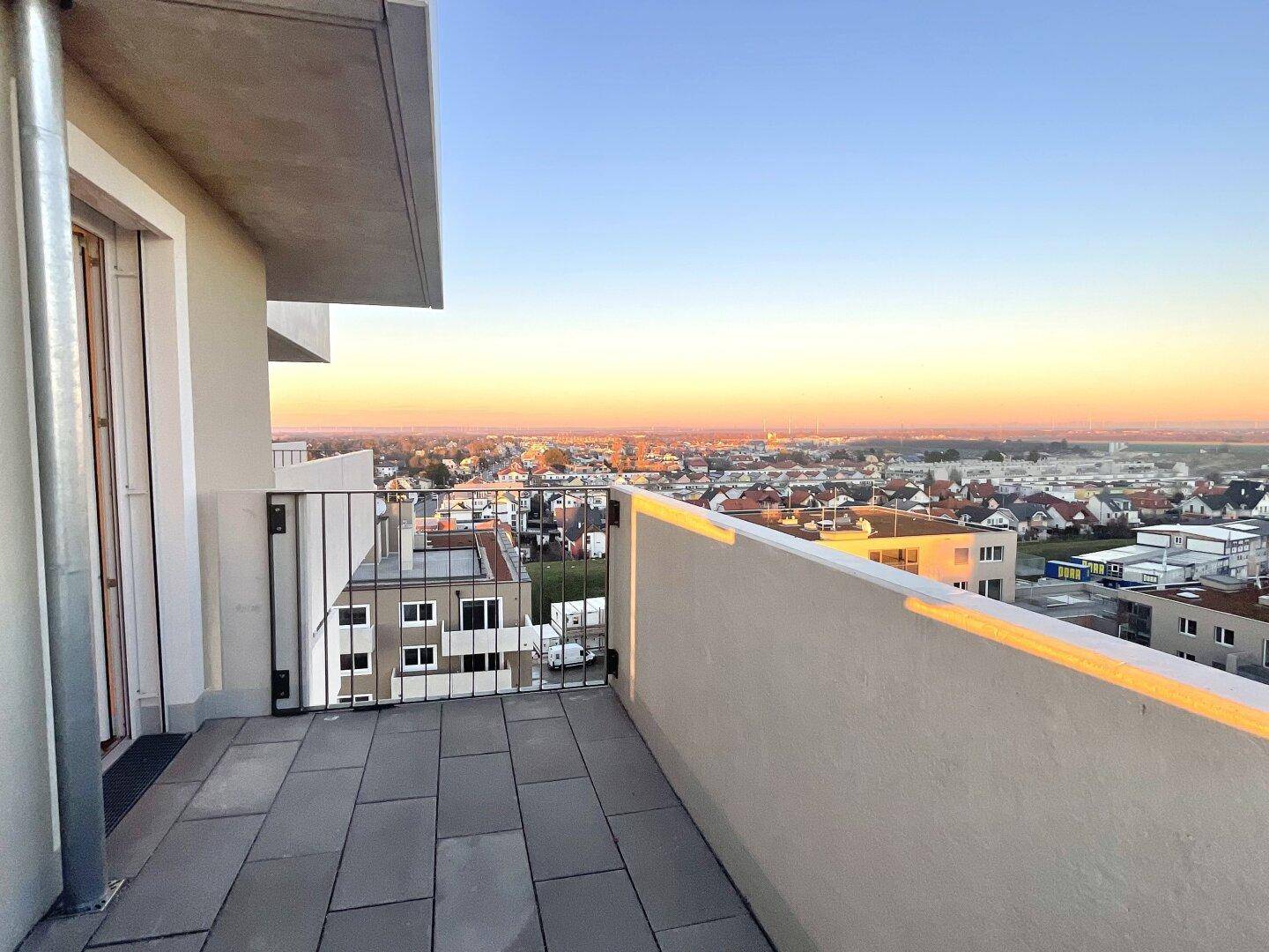 Geräumiger Balkon mit Fliesenboden und weitem Blick über die Stadt bei Sonnenuntergang.