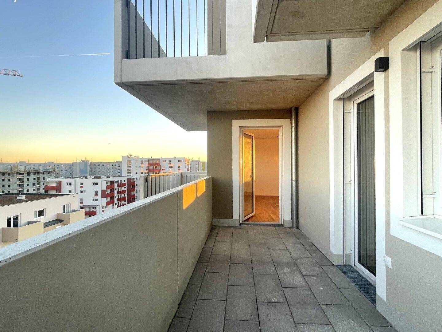 Langer Balkon mit Fliesenboden und Blick auf die umliegenden Gebäude der Wohnanlage.