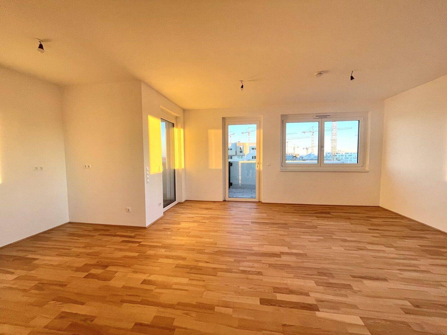Lichtdurchflutetes Wohnzimmer mit hellem Parkettboden und direktem Zugang zum Balkon.