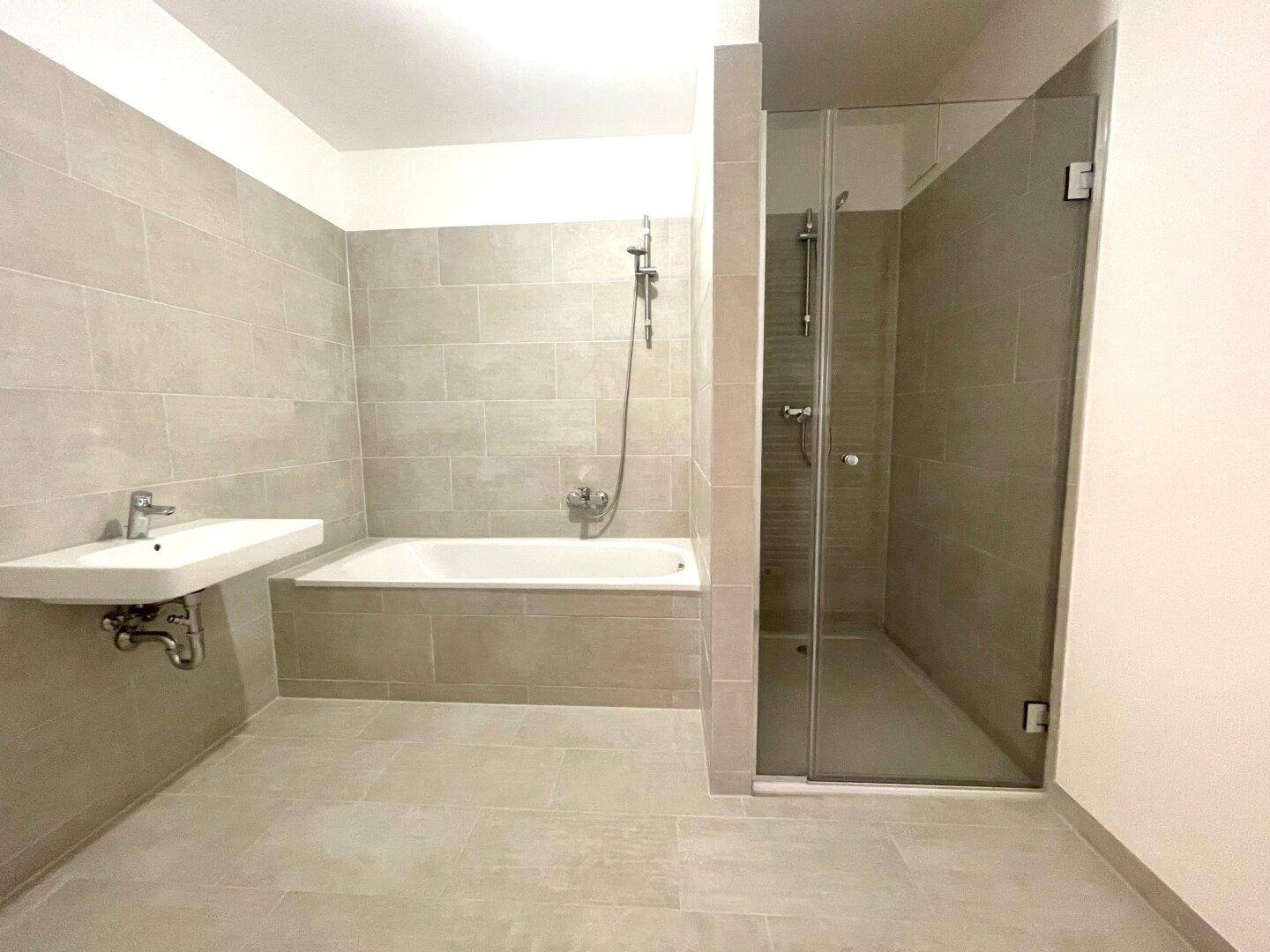 Modernes Badezimmer mit grauen Fliesen, Badewanne, Waschbecken und begehbarer Dusche.
