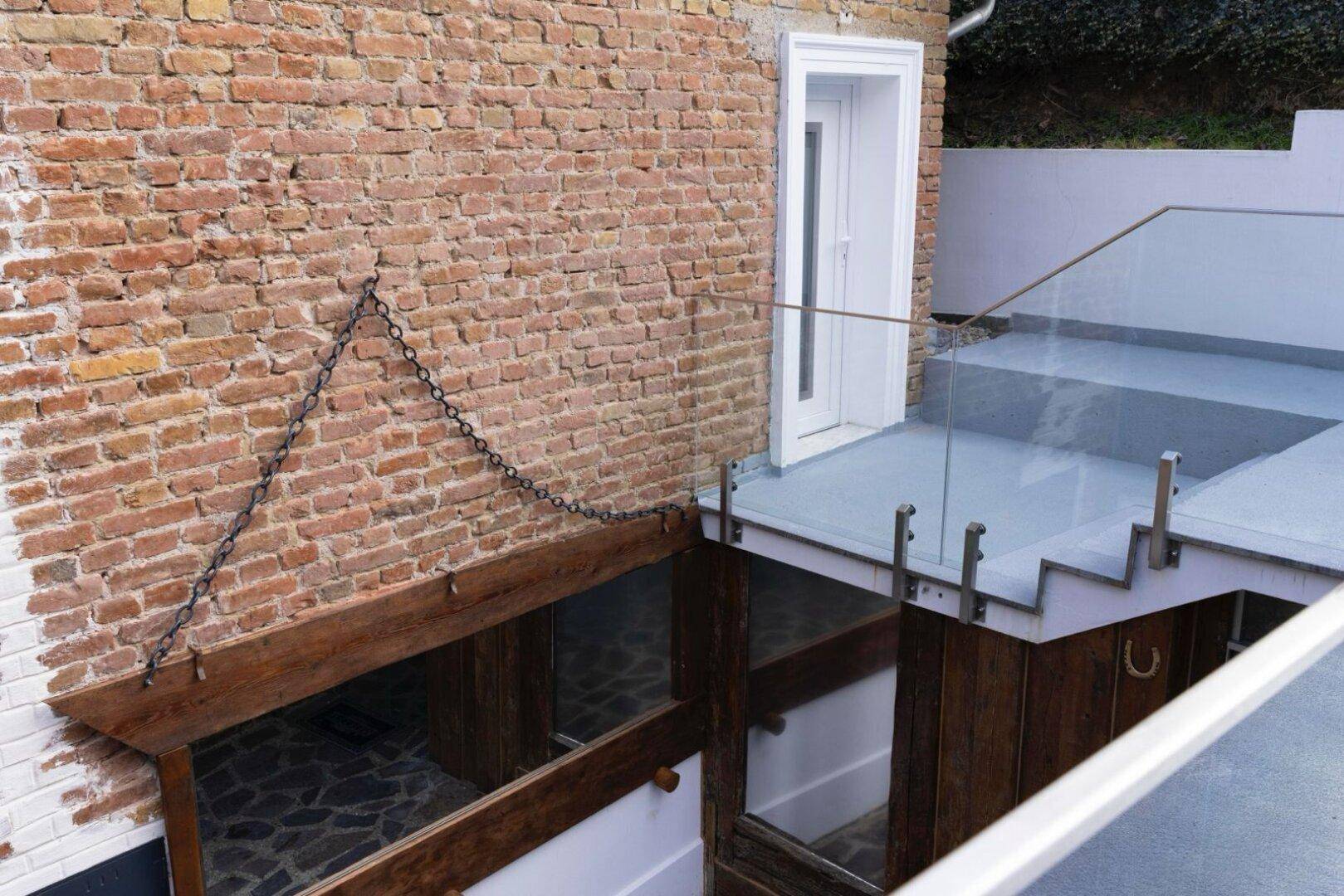 Außentreppe mit Glasgeländer führt zu einem unteren Bereich des Ziegelhauses.