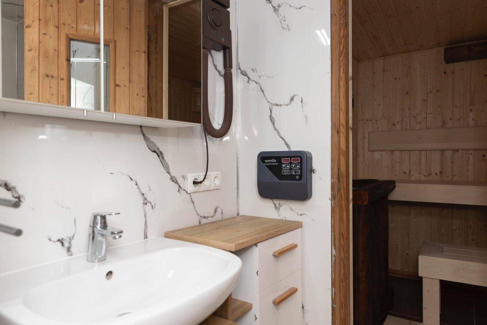 Modernes Badezimmer mit Marmoroptik-Fliesen, Einzelwaschbecken und Zugang zur Sauna.