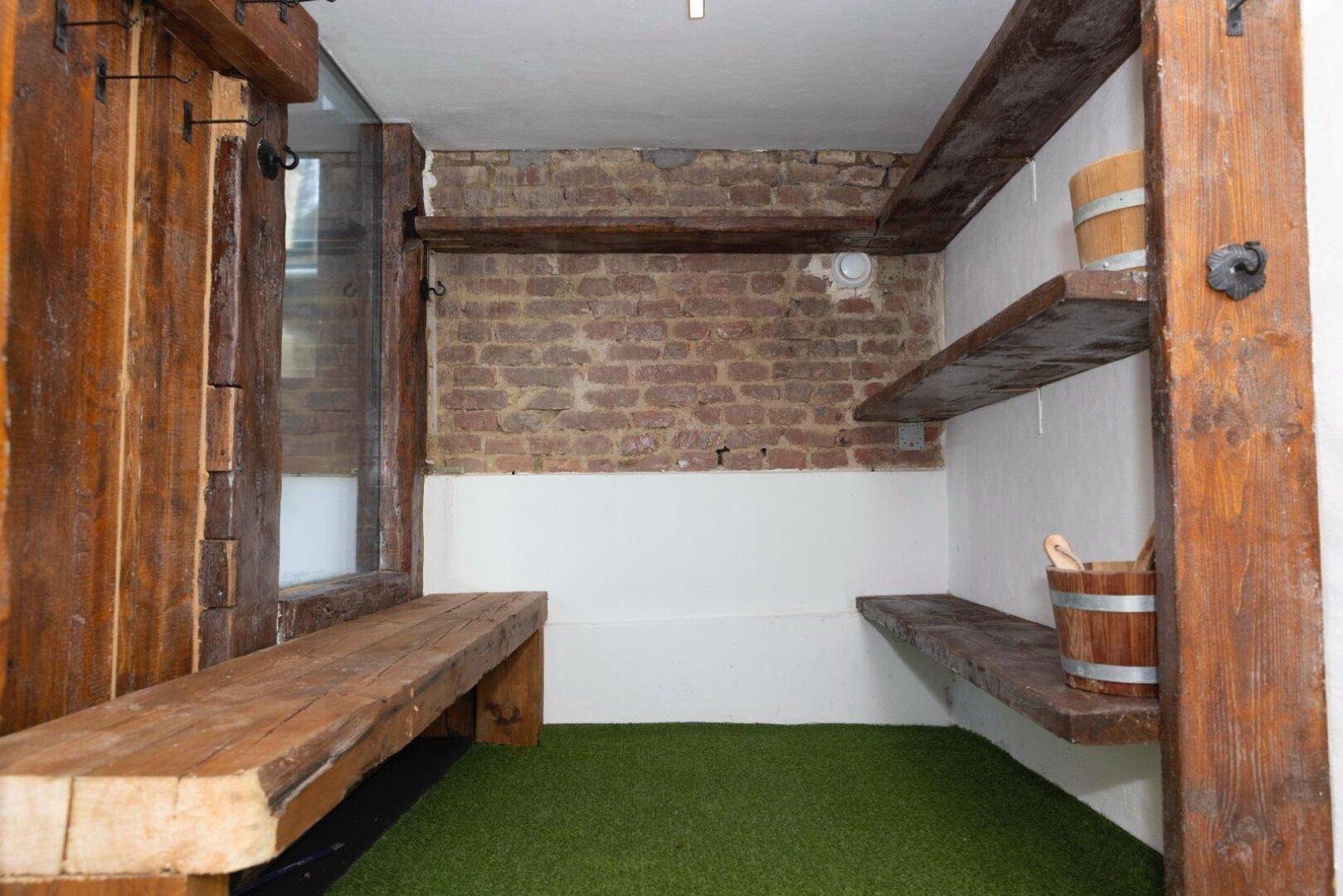 Entspannungsbereich mit Holzbänken, freiliegenden Ziegelwänden und Kunstrasenboden.