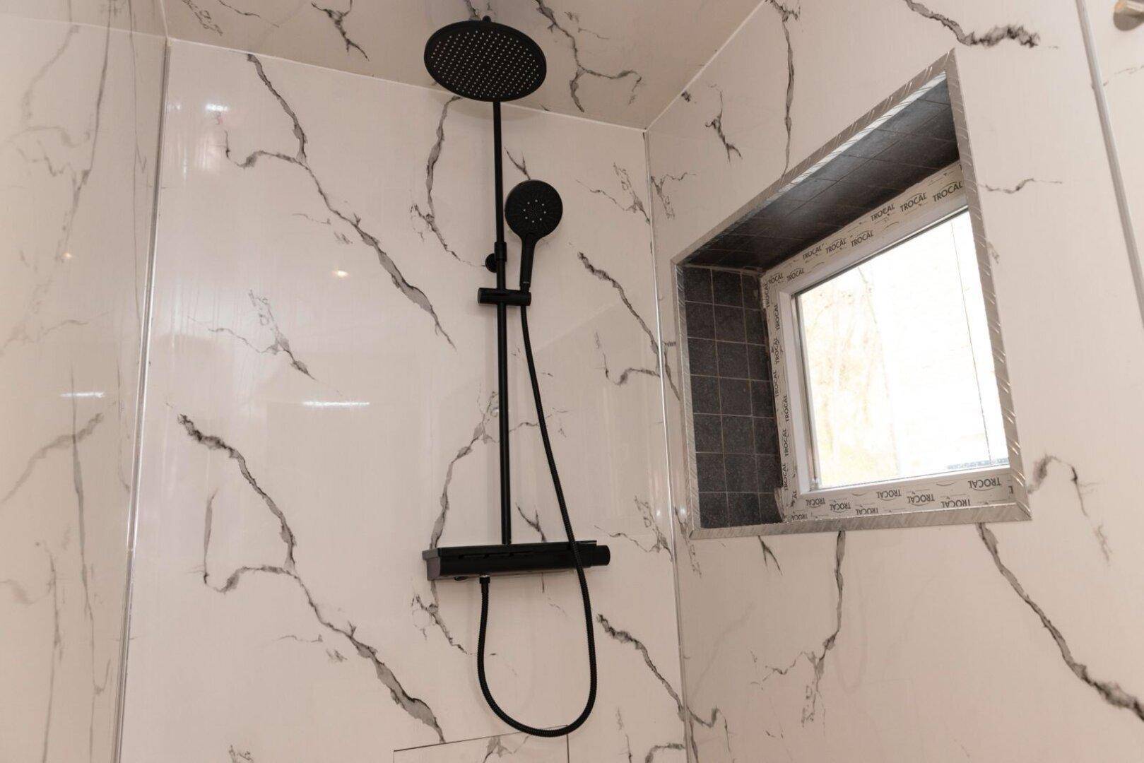 Moderne Duschkabine mit schwarzen Armaturen, Regendusche und Marmoroptik-Fliesen.