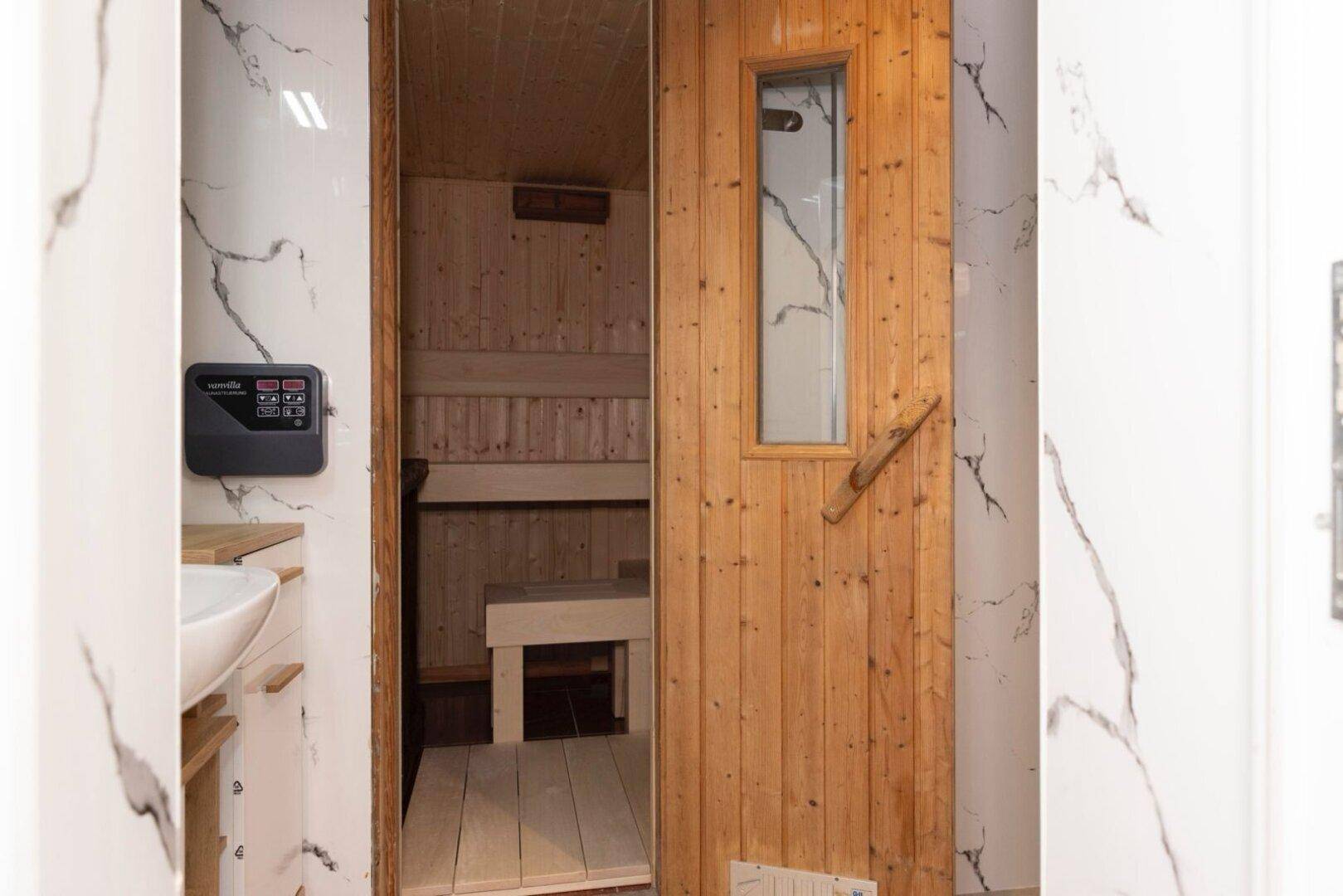 Modernes Badezimmer mit Marmoroptik-Fliesen und Holztür zum Saunabereich.