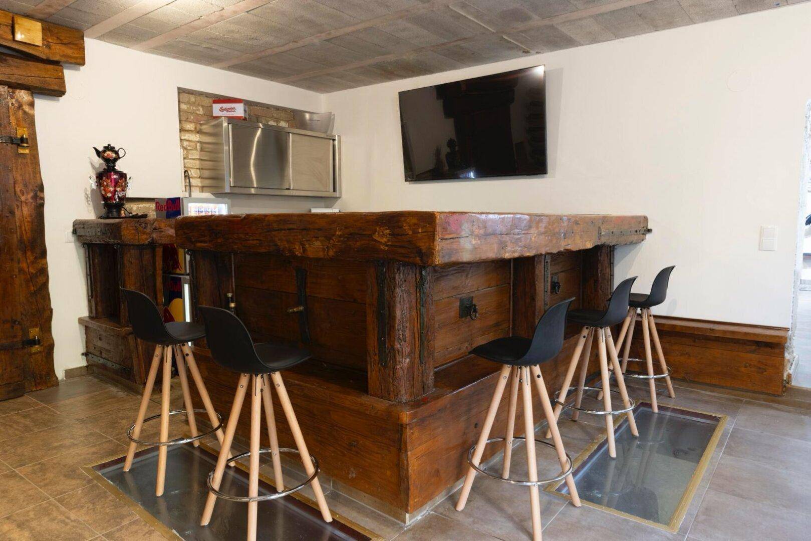Wohnbereich mit großer Holzbar, Flachbildfernseher und modernen Barhockern.