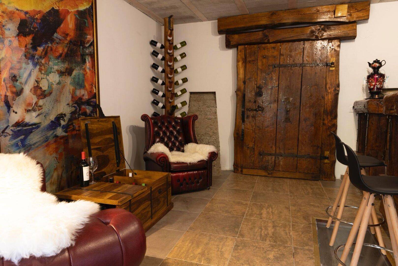 Rustikaler Wohnbereich mit Weinflaschenregal, Ledersessel und massiver Holztür.
