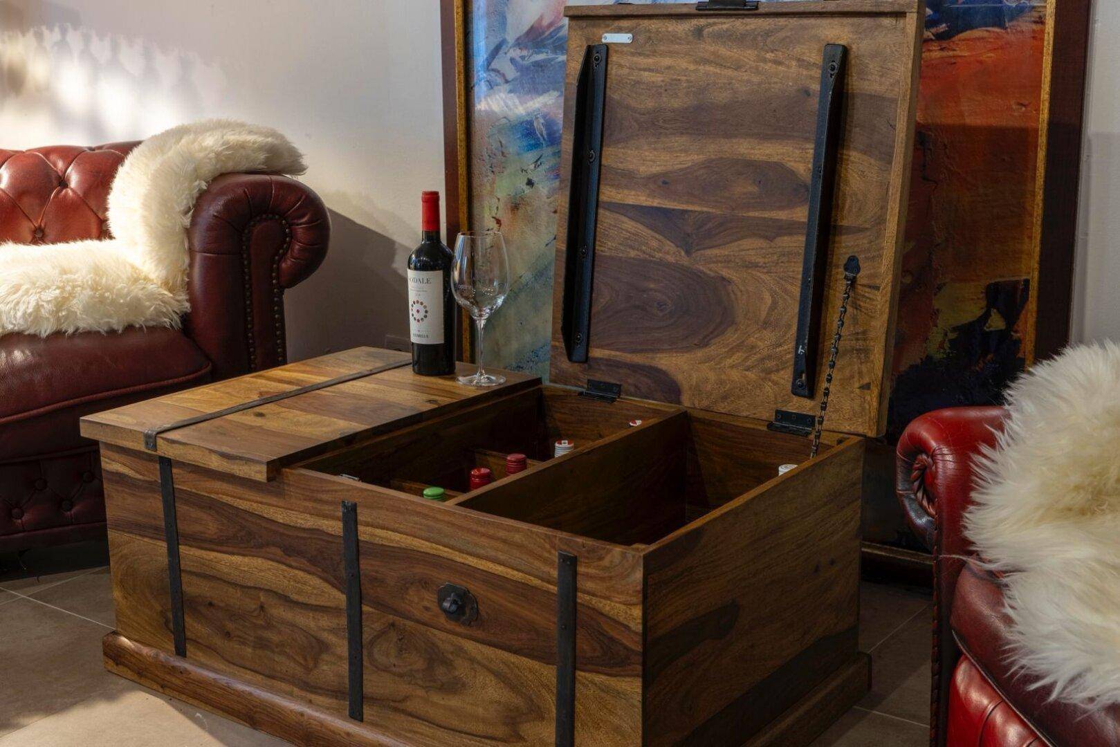 Rustikale Holztruhe als Couchtisch mit Stauraum und Weinflasche.