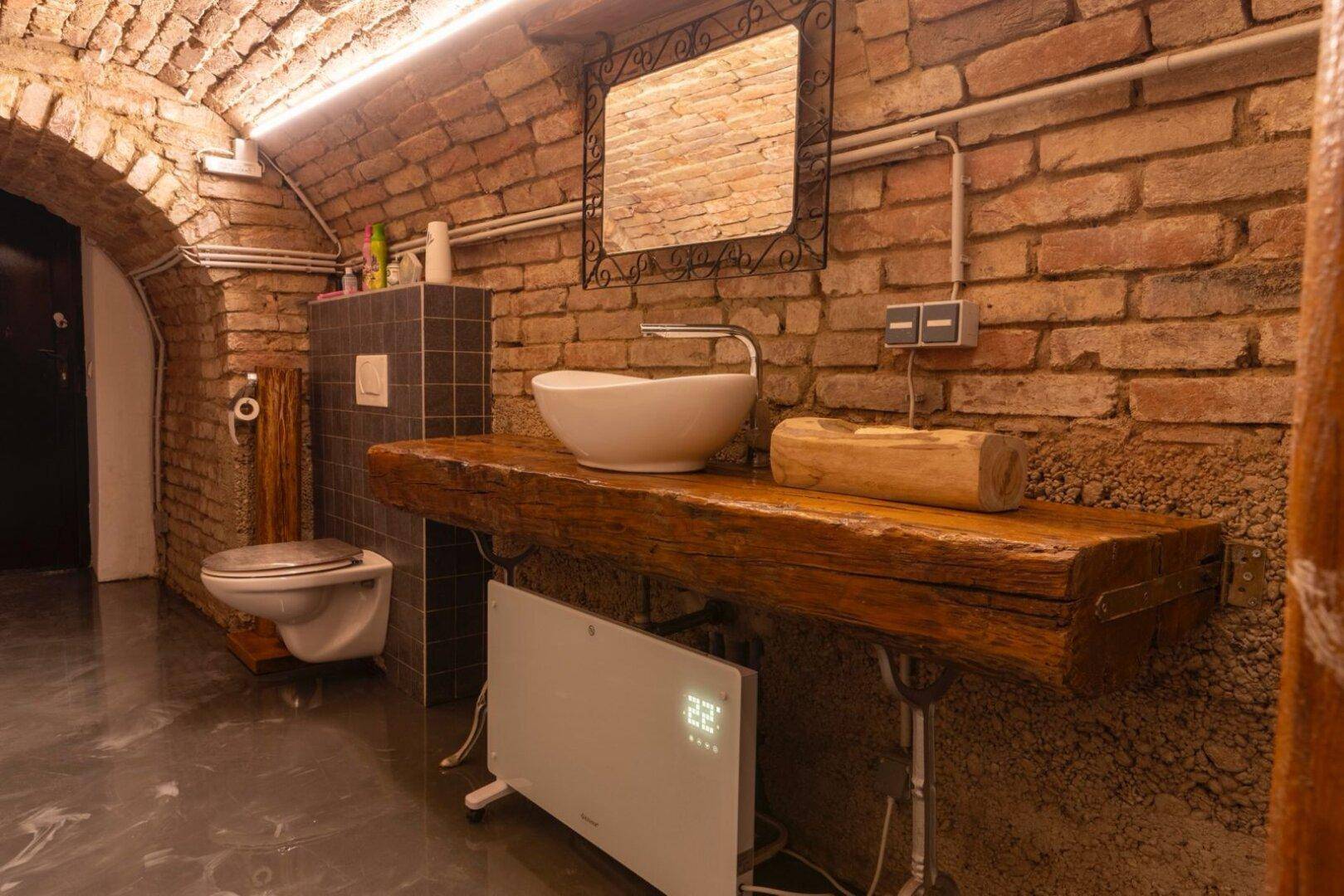 Waschbecken auf rustikaler Holzplatte mit Spiegel und Ziegelwand im Badezimmer.