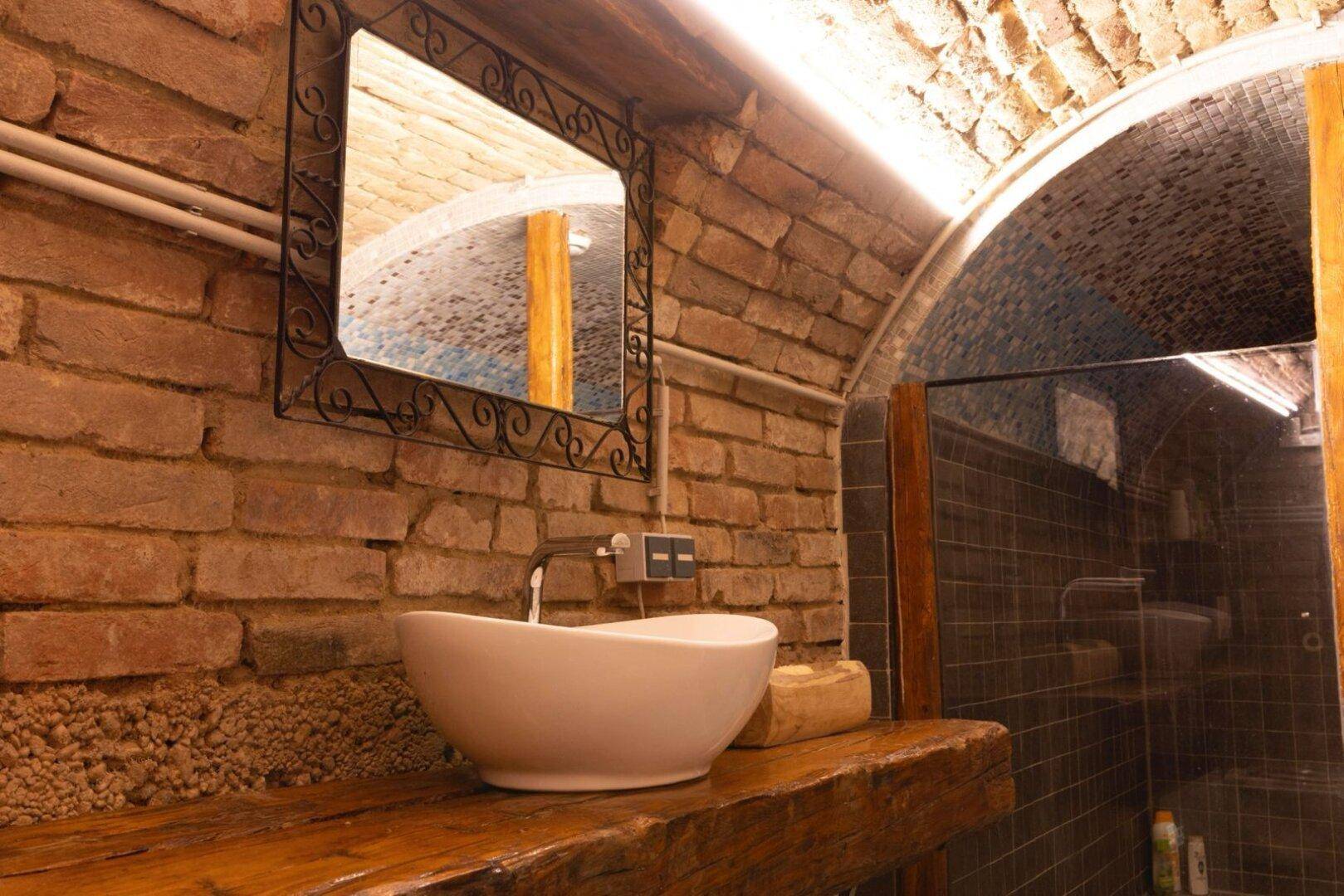 Modernes Waschbecken auf Holzplatte mit Spiegel und Ziegelgewölbedecke.
