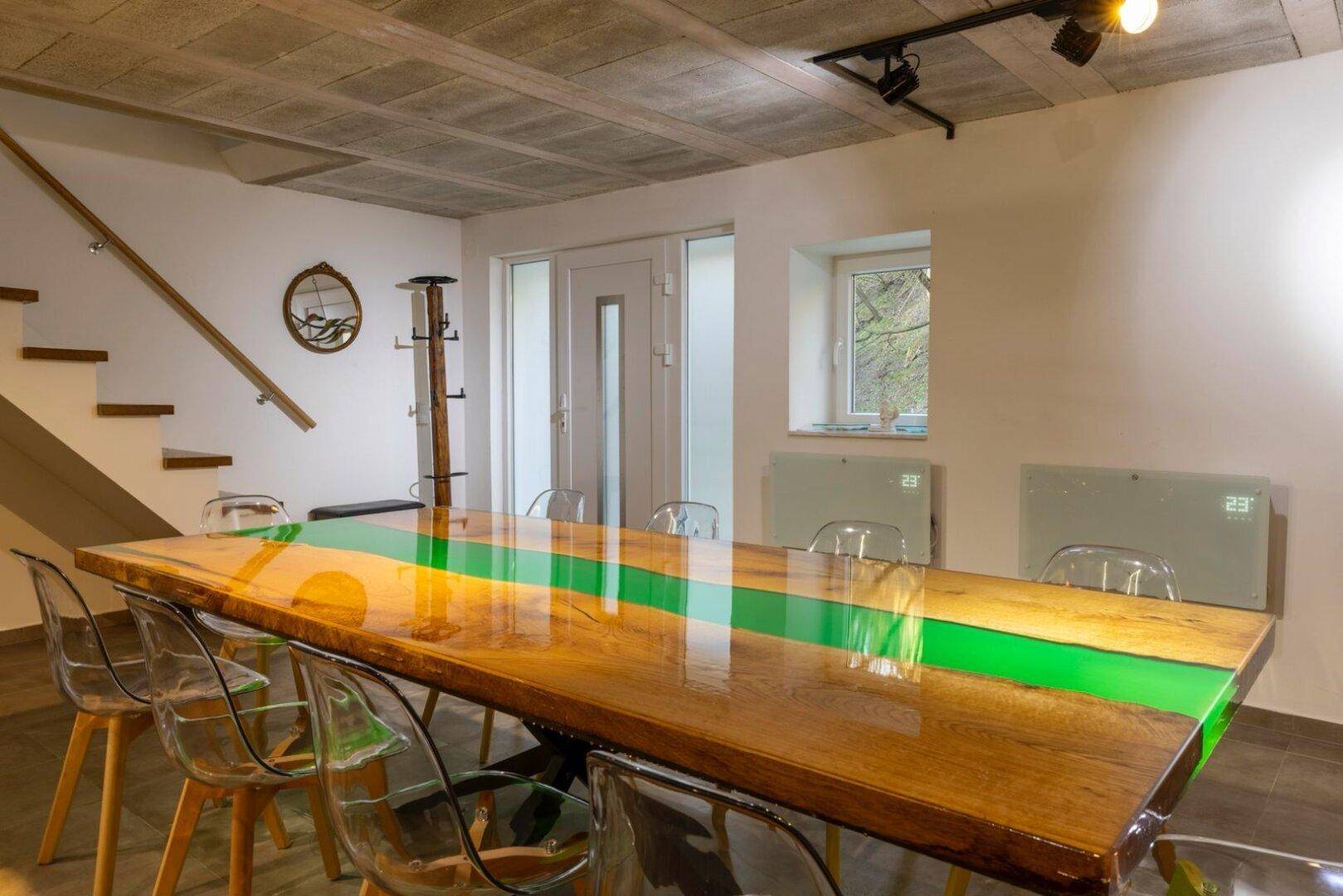 Essbereich mit großem Holztisch, transparenten Stühlen und Treppe zum Obergeschoss.