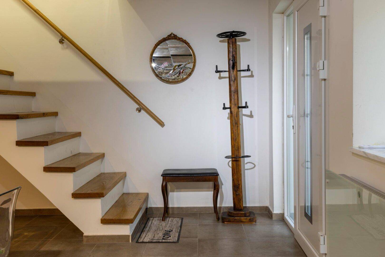 Heller Flurbereich mit Holztreppe, Garderobe und rundem Spiegel.