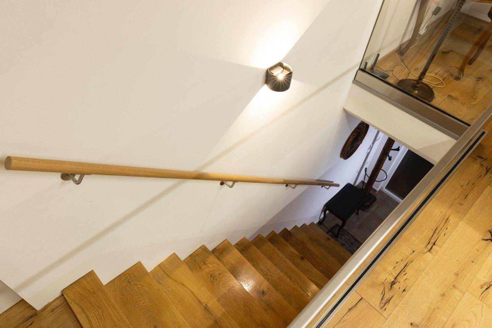 Holztreppe mit Handlauf und Glasgeländer führt in den unteren Wohnbereich.