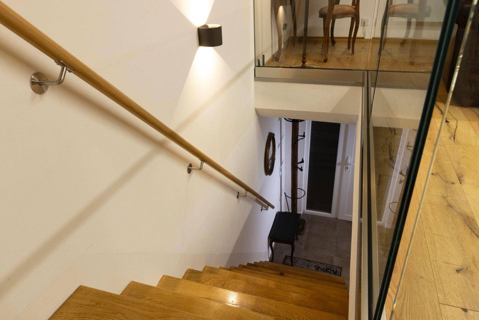 Holztreppe mit Handlauf und Glasgeländer führt in den unteren Wohnbereich.