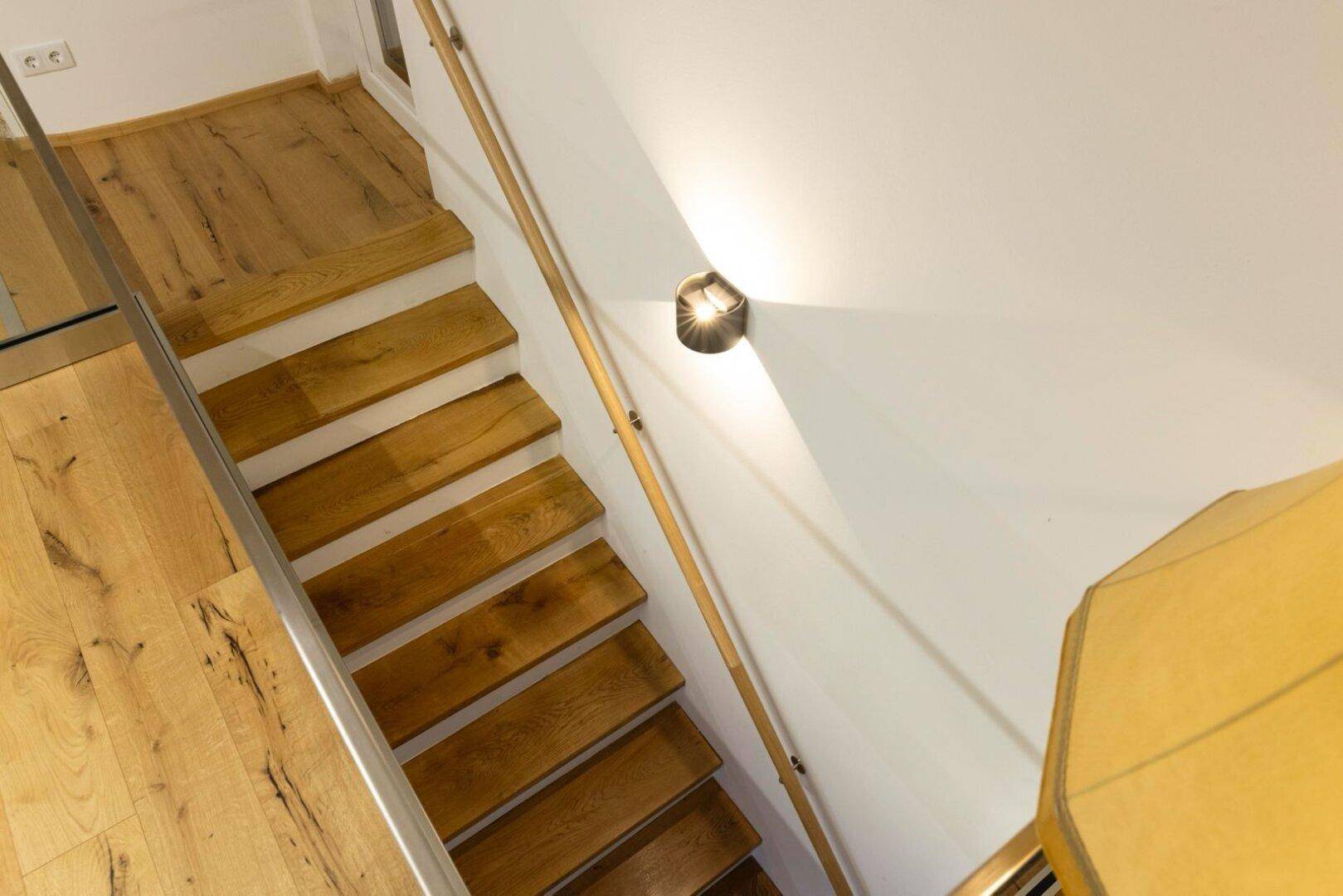 Detailansicht der Holztreppe mit Handlauf und Wandleuchte.