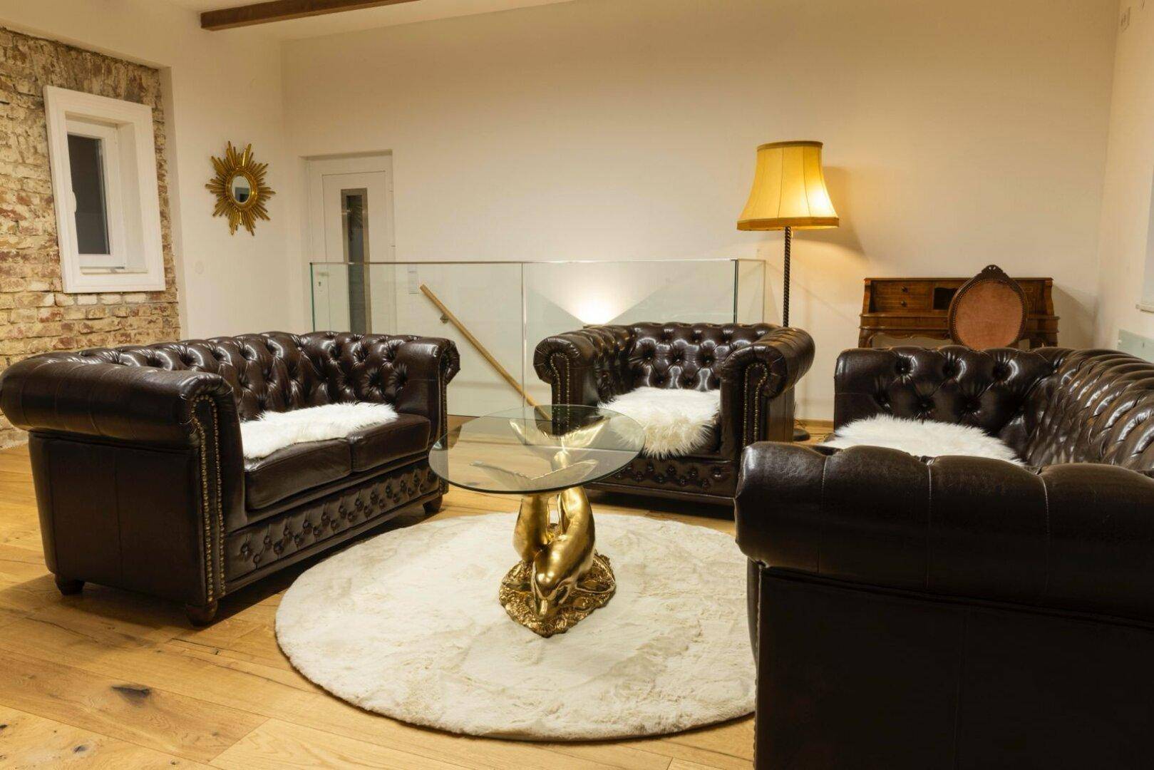 Geräumiges Wohnzimmer mit Ledersofas, rundem Teppich und Glasgeländer.