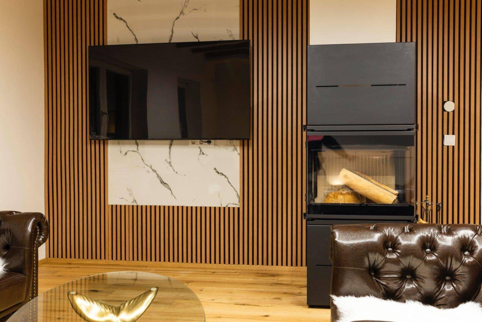 Moderner Kaminofen und Flachbildfernseher an einer Holzlamellenwand.