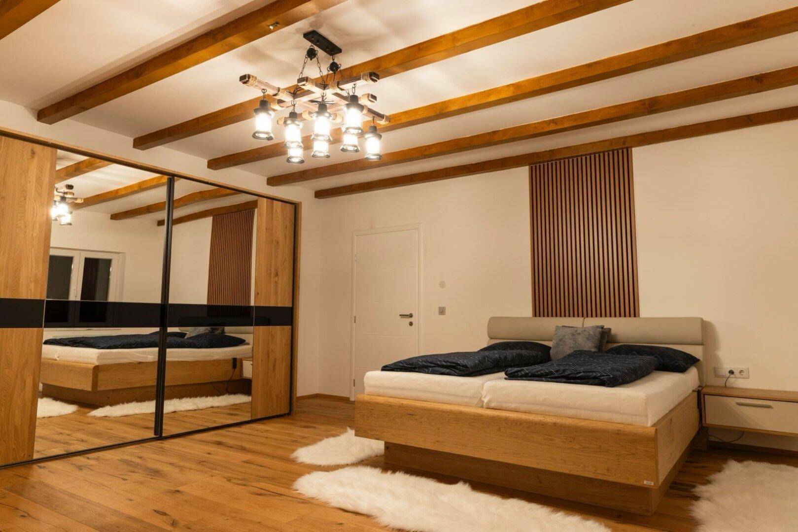 Helles Schlafzimmer mit Holzboden, großem Bett und Spiegelschiebetürenschrank.
