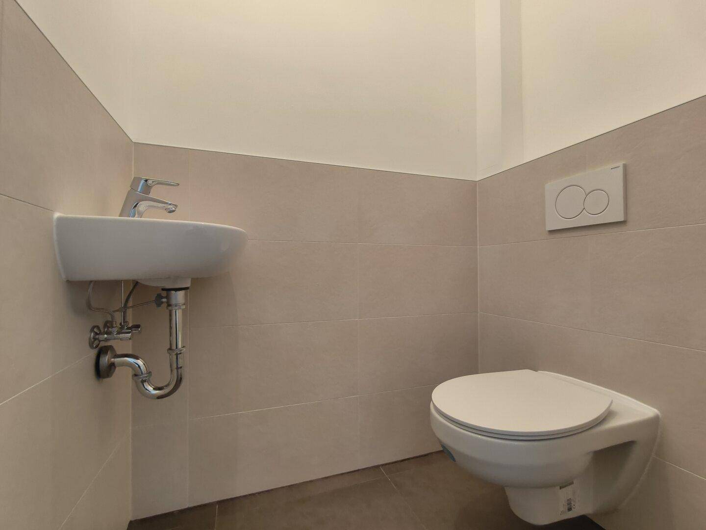 Separates Gäste-WC mit wandhängender Toilette und kleinem Handwaschbecken.