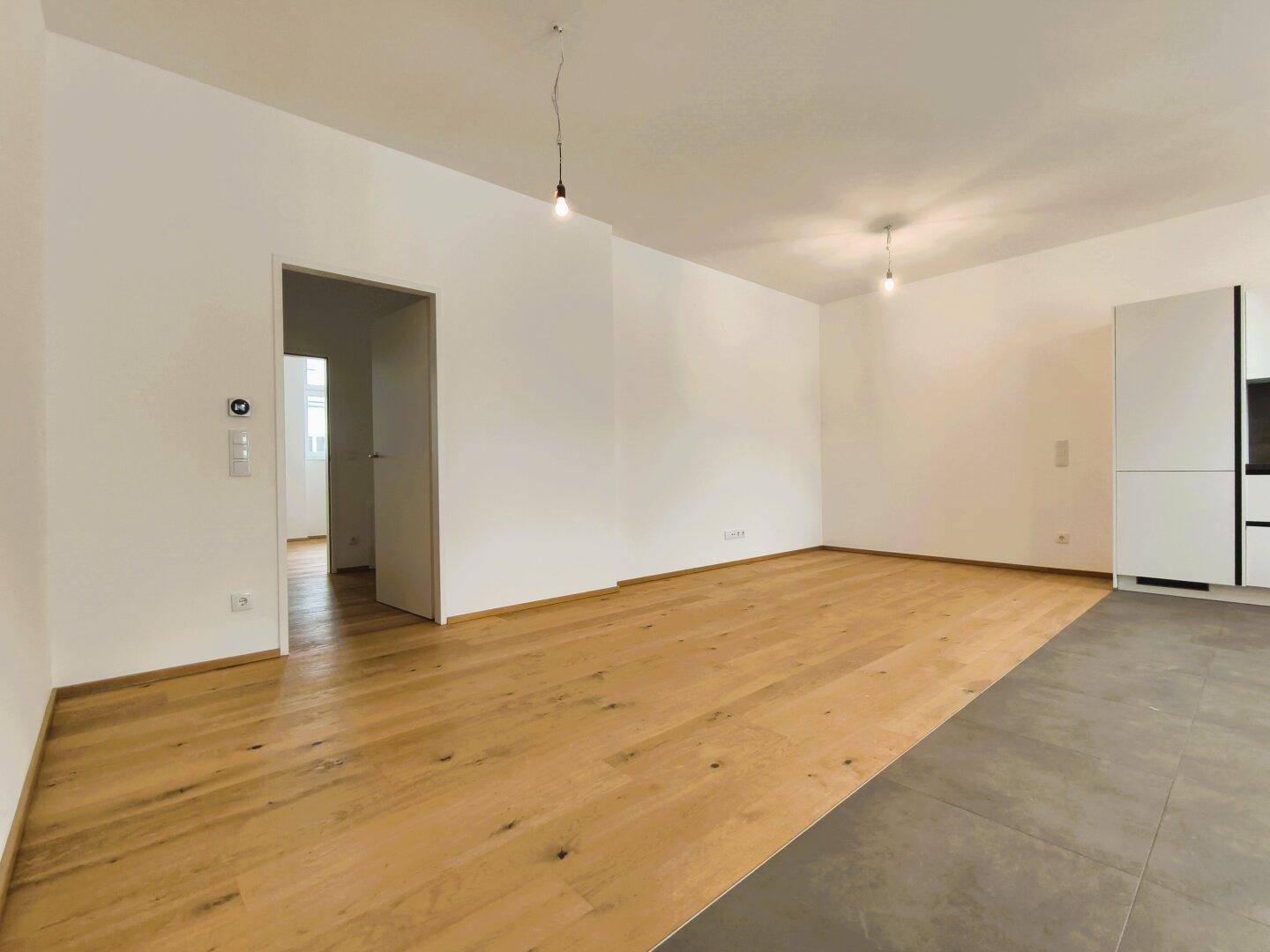 Offener Wohnbereich mit Holzboden und Fliesen, der zu weiteren Räumen führt.
