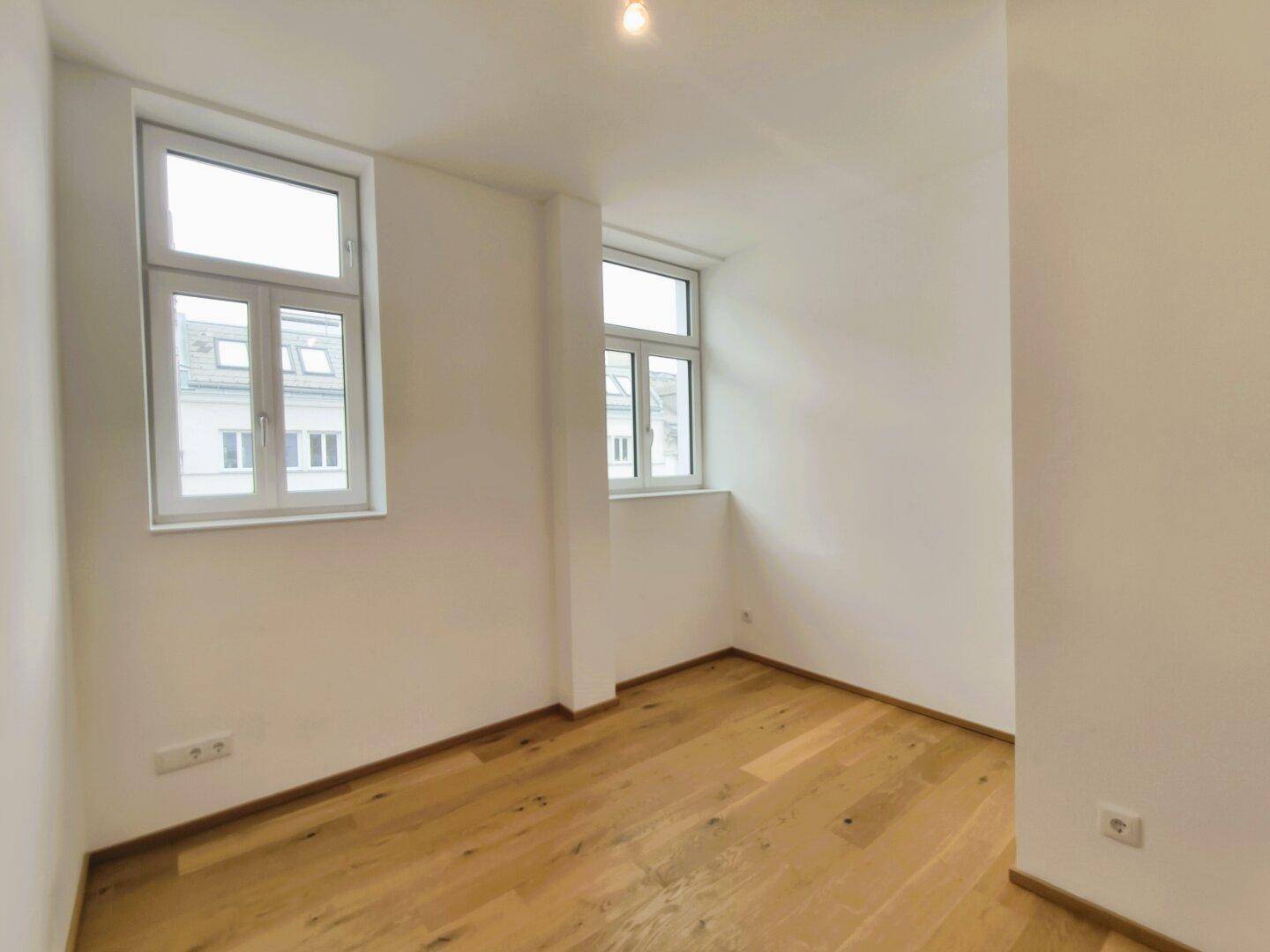 Helles Zimmer mit zwei Fenstern und Holzboden, ideal als Schlaf- oder Arbeitszimmer.