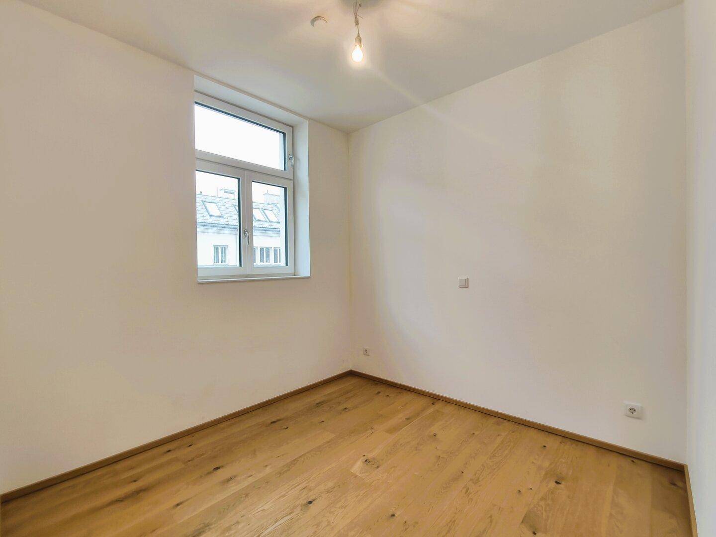 Ruhiges Zimmer mit Holzboden und großem Fenster, vielseitig nutzbar.
