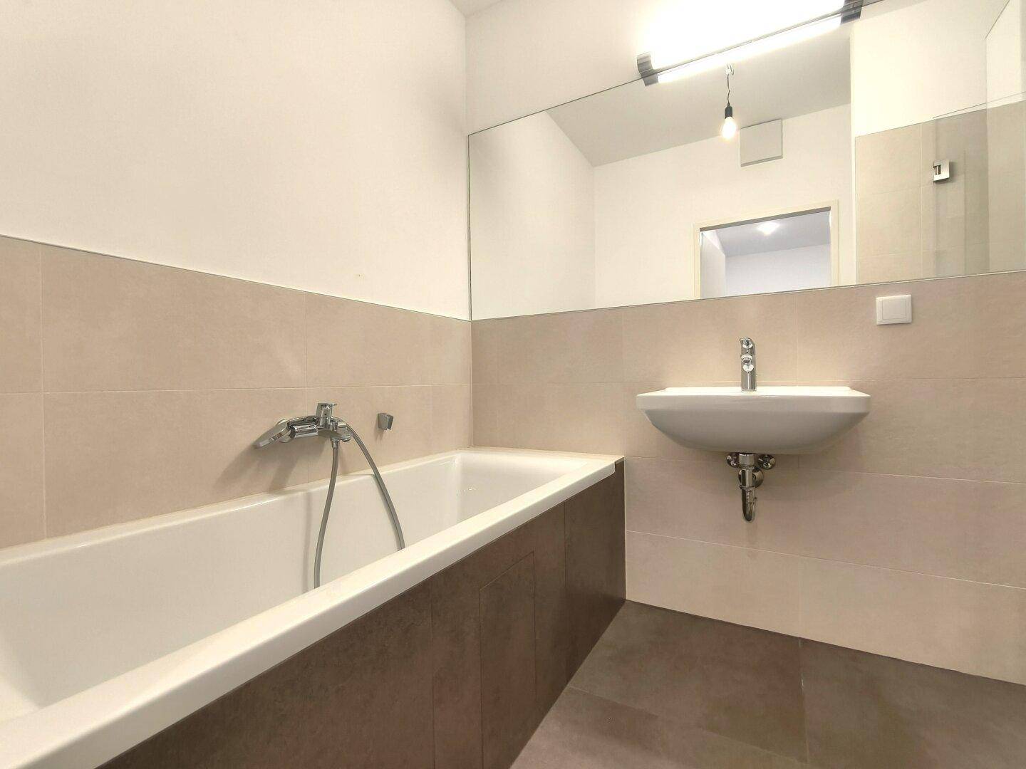 Modernes Badezimmer mit Badewanne, Waschbecken und großen Wandfliesen.