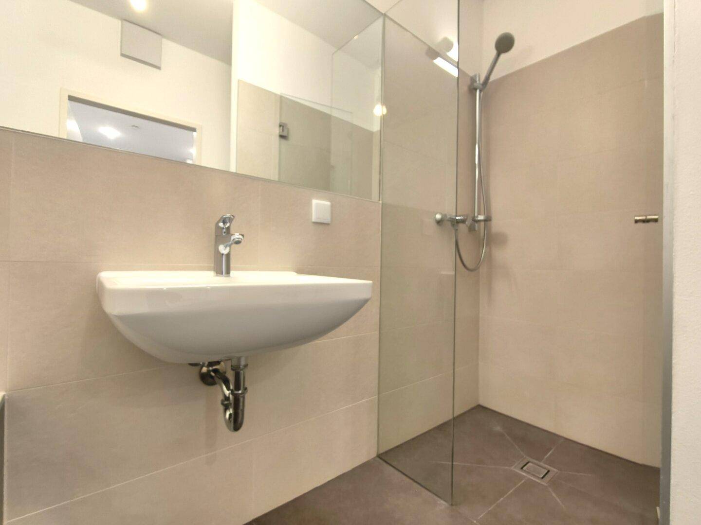 Zeitgemäßes Badezimmer mit ebenerdiger Dusche, Waschbecken und großem Spiegel.