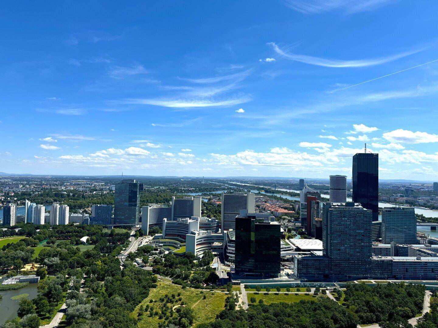 Beeindruckende Luftaufnahme einer modernen Skyline mit Hochhäusern, weitläufigen Parks und einem Fluss.