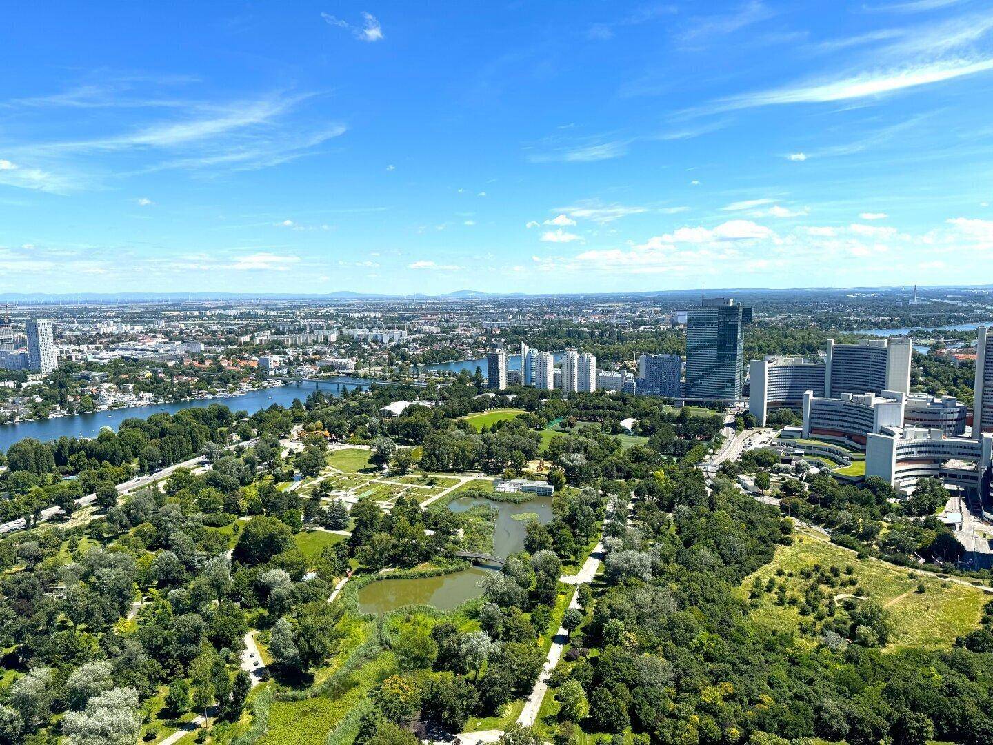 Panoramablick aus der Vogelperspektive auf einen großen Stadtpark, einen Fluss und moderne Hochhäuser.